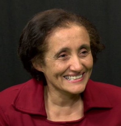 Professora Ester Sabino sorri em perfil. Usa camisa vermelho escuro com gola