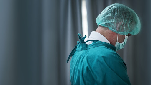 Foto de um profissional da saúde usando uniforme verde água virado de lado e olhando para baixo.